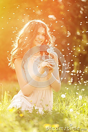 Young spring fashion woman blowing dandelion in spring garden. S Stock Photo