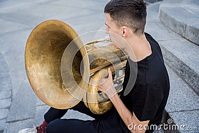 Young street musician playing tuba sitting on granite steps Stock Photo