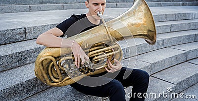 Young street musician playing tuba sitting on granite steps Stock Photo