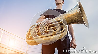 Young street musician playing tuba at the sunset sky background. Stock Photo