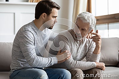 Young stressed man comforting irritated mature old father. Stock Photo