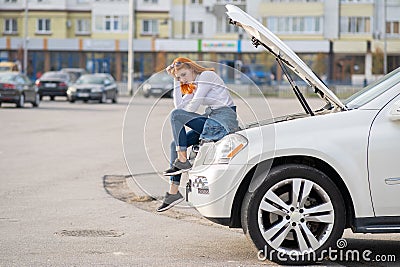 Young stressed woman driver near broken car with popped hood waiting for assistance Stock Photo