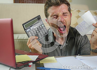 Young stressed and worried man at home living room using calculator and laptop doing domestic accounting paperwork screaming crazy Stock Photo