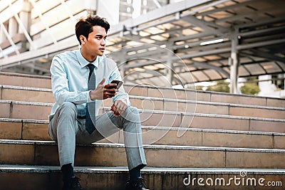 Young Striving Asian Businessman Sitting on Staircase in the City. Using Mobile Phone Stock Photo