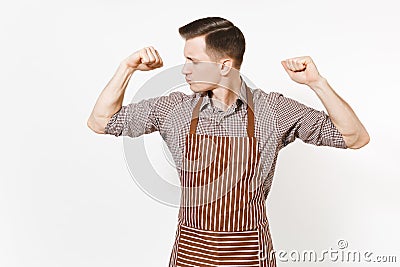 Young strong man chef or waiter in striped brown apron, shirt showing biceps, muscles isolated on white background. Male Stock Photo
