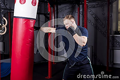 Young strong mixed martial arts fighter delivers strong hand punch to punching bag. Active exercise in gym. Stock Photo