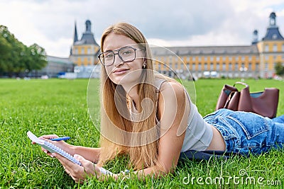 Young student girl lying on grass, educational building background Stock Photo