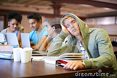 Studying bores him. A young student looking bored while in his classmates study int the background. Stock Photo