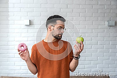 Young student man doubts what to choose healthy food or sweets junk unhealthy food holding green apple and donuts in hands Stock Photo