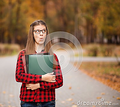 Young student with surprised face looks out of folder in red checkered shirt. Portrait of clever young woman Stock Photo