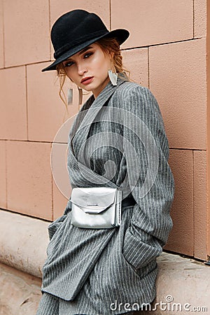 Young stylish beautiful woman fashion model is posing in street, wearing pantsuit, having purse on her waist Stock Photo