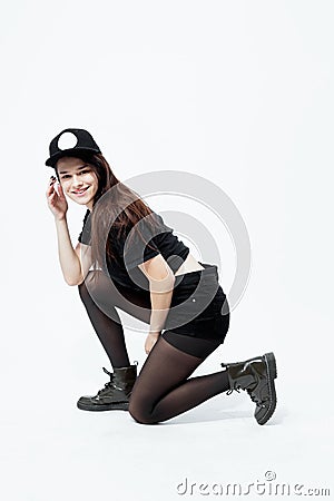 Young stylish dark-haired girl dressed in a black top, shorts, tights and cap sits in a squat on the white background in Stock Photo