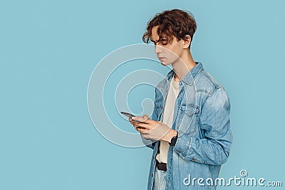 Freestyle. Man in denim shirt standing isolated on gray chatting on smartphone concentrated Stock Photo