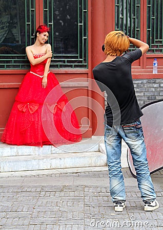 Young stylish photographer taking a picture of a beautiful girl in red dress for wedding portfolio Editorial Stock Photo