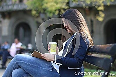 Young stylish woman in the city, sitting on a bench, reading and drinking coffee Stock Photo