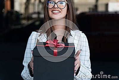 Young stylish woman hands gift. Happy young woman holds gift box and smiling. Black gift box with red bow Stock Photo