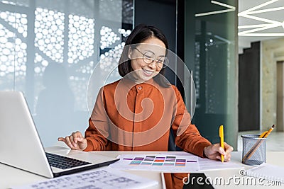 Young successful asian financier working inside office with papers, businesswoman behind paperwork joyfully recording Stock Photo