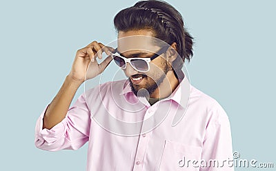 Young successful Indian man adjusts sunglasses and smiles self-confidently standing in studio Stock Photo