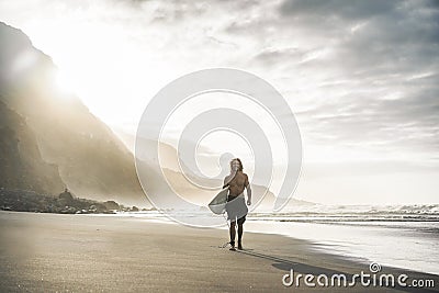 Young surfer on tropical beach at sunset - Man guy with his surf board walking next the ocean on sunny day - Extreme sport concept Stock Photo