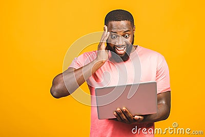 Young surprised african man standing and using laptop computer isolated over yellow background Stock Photo