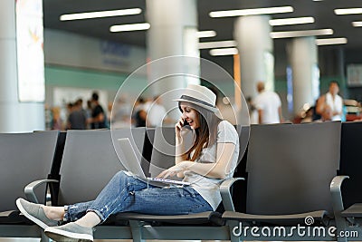 Young surprised traveler tourist woman working on laptop talk on mobile phone call friend booking taxi hotel wait in Stock Photo