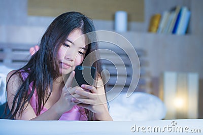 Young sweet and beautiful Asian Chinese 20s or 30s woman smiling happy lying on bed using internet mobile phone dating or sending Stock Photo