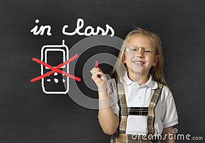 Young sweet junior schoolgirl writing with chalk about not using mobile phone in school class Stock Photo