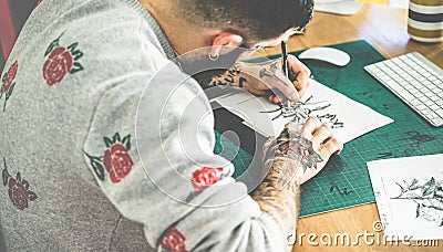 Young tattoo artist drawing sketch inside ink studio - Hipster tattoer at work - Contemporary skin trends generation - - Focus on Stock Photo