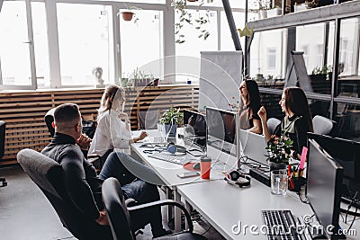 Young team works in a spacious light modern open space office sitting at a desks with a computer and laptops Stock Photo