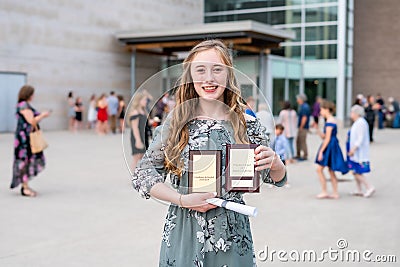 Young Teen Girl/Middle School student standing in front of school with awards and diploma after Grade 8/Middle school graduation c Stock Photo