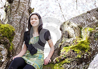 Young teen girl sitting on branches of flowering cherry tree Stock Photo