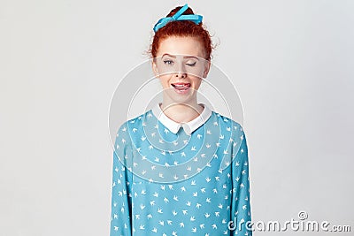 Young teenage girl with ginger hair knot sticking out her tongue having funny look over gray background. Stock Photo