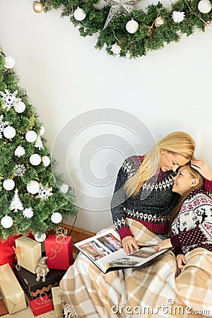 Young teenage girl resting her head on mother`s chest, hugging each other and looking through family photo album on Christmas day Stock Photo