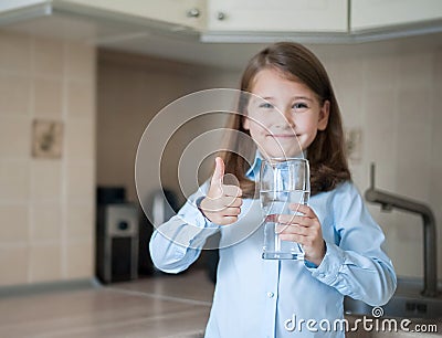 Young teenager girl showing thumbs up sign and holding a transparent glass. Child recommend drinking water. Good healthy habit for Stock Photo