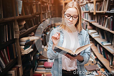 Young teenager is in public library. She has found a book and read it. This girl is calm peaceful and thoughtful. Stock Photo
