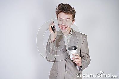 Young teenager with surprised emotions in grey business clothes standing with mobile phone and paper cup of coffee on white studio Stock Photo