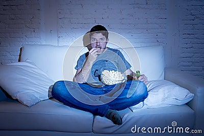 Young television addict man sitting on home sofa watching TV eating popcorn and drinking beer bottle Stock Photo