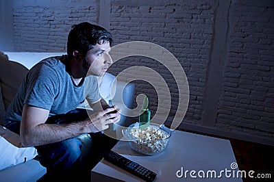 Young television addict man sitting on home sofa watching TV eating popcorn and drinking beer bottle Stock Photo