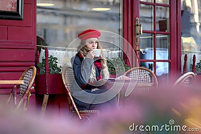 Girl in a red beret sits at a table and drinks coffee in a street cafe Stock Photo