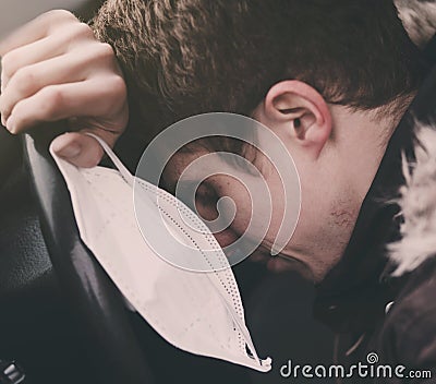 Young tired man in a car, looking worried, holding a medical mask Stock Photo