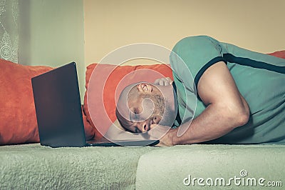 Young tired man taking a break and fell asleep on the bed with his lap top computer after hard and long online work, dark image Stock Photo