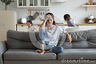 Exhausted mother sitting on couch while kids running at home Stock Photo