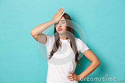 Young tired woman in white t-shirt, sighing and making facepalm to express annoyance, feeling fed up and tensed Stock Photo