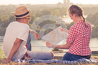 Couple of tourists sitting on hill and using map to find next location Stock Photo