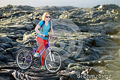 Young tourist cycling on lava field on Hawaii. Female hiker heading to lava viewing area at Kalapana on her bike. Tourist on hike Stock Photo