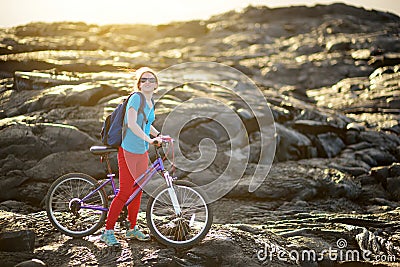 Young tourist cycling on lava field on Hawaii. Female hiker heading to lava viewing area at Kalapana on her bike. Tourist on hike Stock Photo