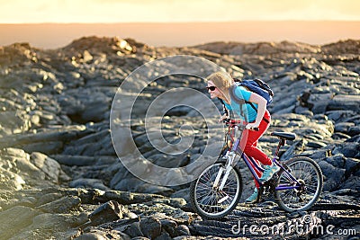 Young tourist cycling on lava field on Hawaii. Female hiker heading to lava viewing area at Kalapana on her bike. Tourist on hike Stock Photo