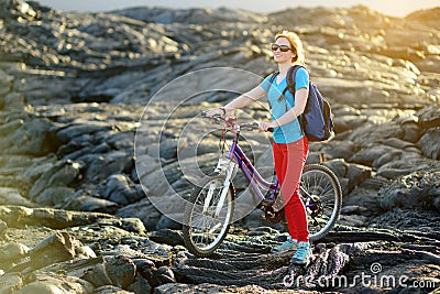 Young tourist cycling on lava field on Hawaii. Female hiker heading to lava viewing area at Kalapana on her bike. Tourist on hike Stock Photo