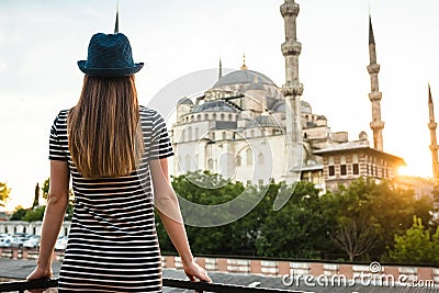 A young tourist girl with a beautiful figure looks from the hotel terrace to the world famous blue mosque Sultanahmet in Stock Photo