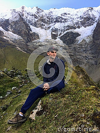 A young tourist sitting in front of the glorious Humantay Lake, high in the Andes Mountains, along the Salkantay Trail in Peru Stock Photo